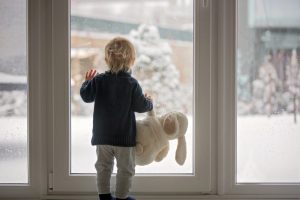 child-with-toy-rabbit-looking-out-the-window-at-the-snow